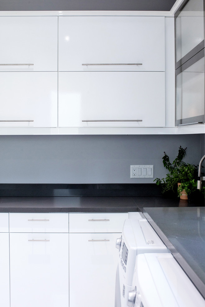 Exempel på en stor modern grå l-formad grått tvättstuga enbart för tvätt, med en undermonterad diskho, släta luckor, vita skåp, bänkskiva i kvarts, grå väggar, marmorgolv, en tvättmaskin och torktumlare bredvid varandra och vitt golv