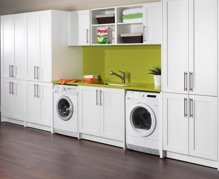 Photo of a large contemporary single-wall utility room in San Francisco with recessed-panel cabinets, white cabinets, laminate countertops, green walls, dark hardwood flooring, a side by side washer and dryer and a submerged sink.