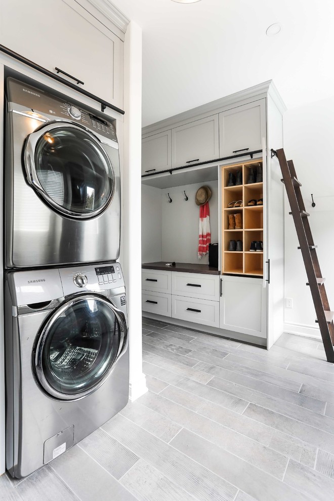 Modelo de lavadero multiusos grande con armarios estilo shaker, suelo de baldosas de porcelana, lavadora y secadora apiladas y puertas de armario blancas