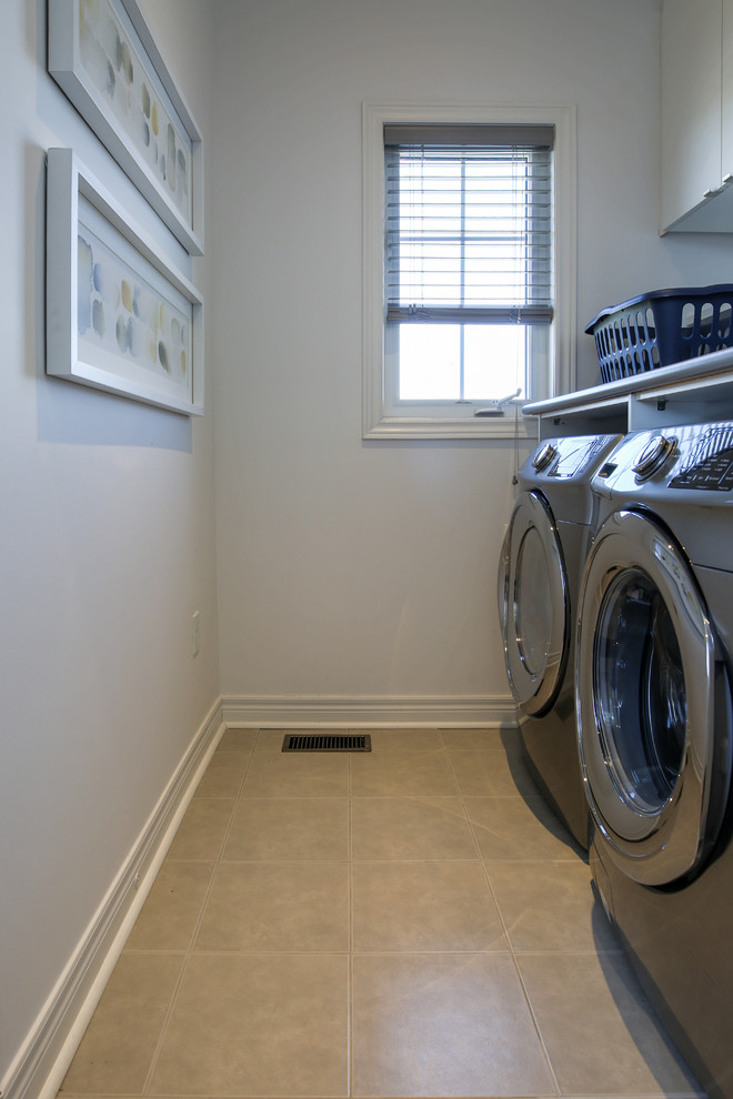Bild på en liten vintage grå parallell grått tvättstuga enbart för tvätt, med släta luckor, vita skåp, laminatbänkskiva, vita väggar, klinkergolv i porslin och en tvättmaskin och torktumlare bredvid varandra