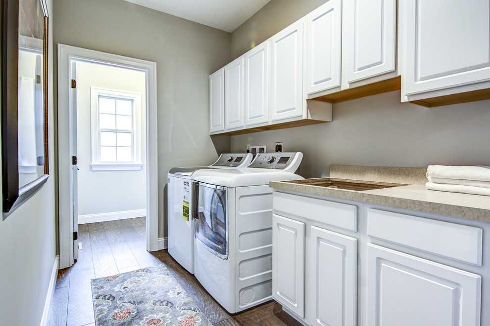 Photo of a small classic single-wall separated utility room in Other with a submerged sink, raised-panel cabinets, white cabinets, laminate countertops, beige walls, dark hardwood flooring, a side by side washer and dryer and beige worktops.