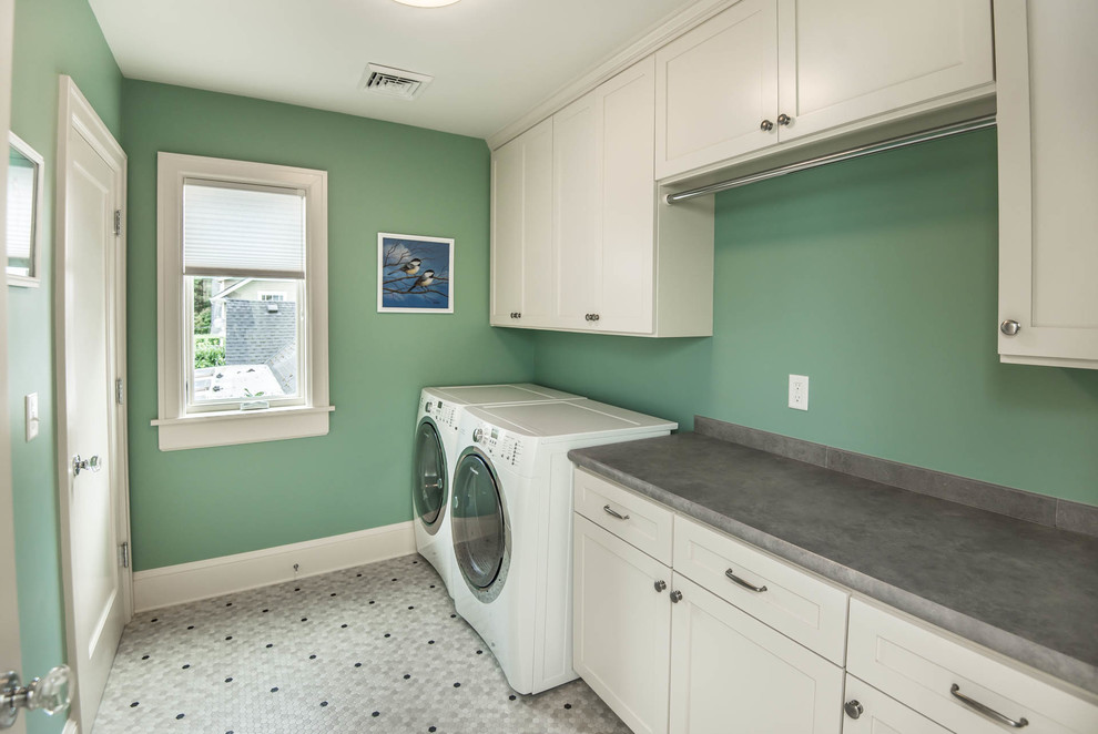 Exempel på en stor klassisk parallell tvättstuga enbart för tvätt, med skåp i shakerstil, vita skåp, laminatbänkskiva, gröna väggar, vinylgolv och en tvättmaskin och torktumlare bredvid varandra