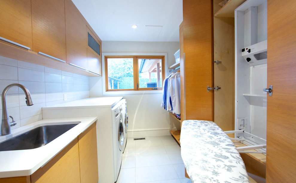 Immagine di una grande sala lavanderia minimal con lavello sottopiano, ante lisce, ante in legno scuro, pareti bianche, pavimento con piastrelle in ceramica e lavatrice e asciugatrice affiancate
