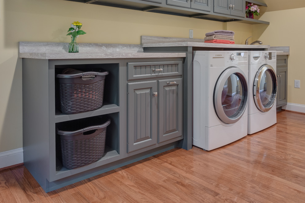 Foto di una lavanderia multiuso tradizionale con lavello da incasso, ante grigie, pavimento in legno massello medio, lavatrice e asciugatrice affiancate, ante con bugna sagomata e pareti beige