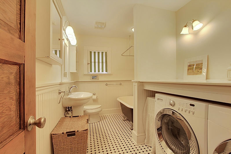 Example of a mid-sized farmhouse single-wall porcelain tile utility room design in New Orleans with wood countertops, white walls and a side-by-side washer/dryer