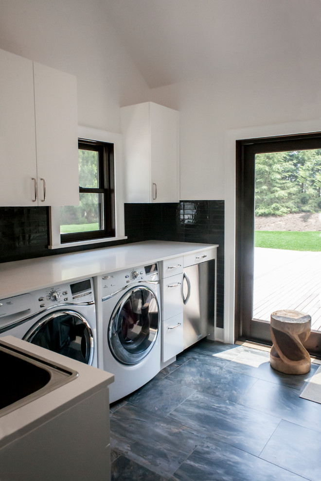 Klassische Waschküche in L-Form mit Einbauwaschbecken, flächenbündigen Schrankfronten, weißen Schränken, weißer Wandfarbe, Waschmaschine und Trockner nebeneinander und weißer Arbeitsplatte in New York