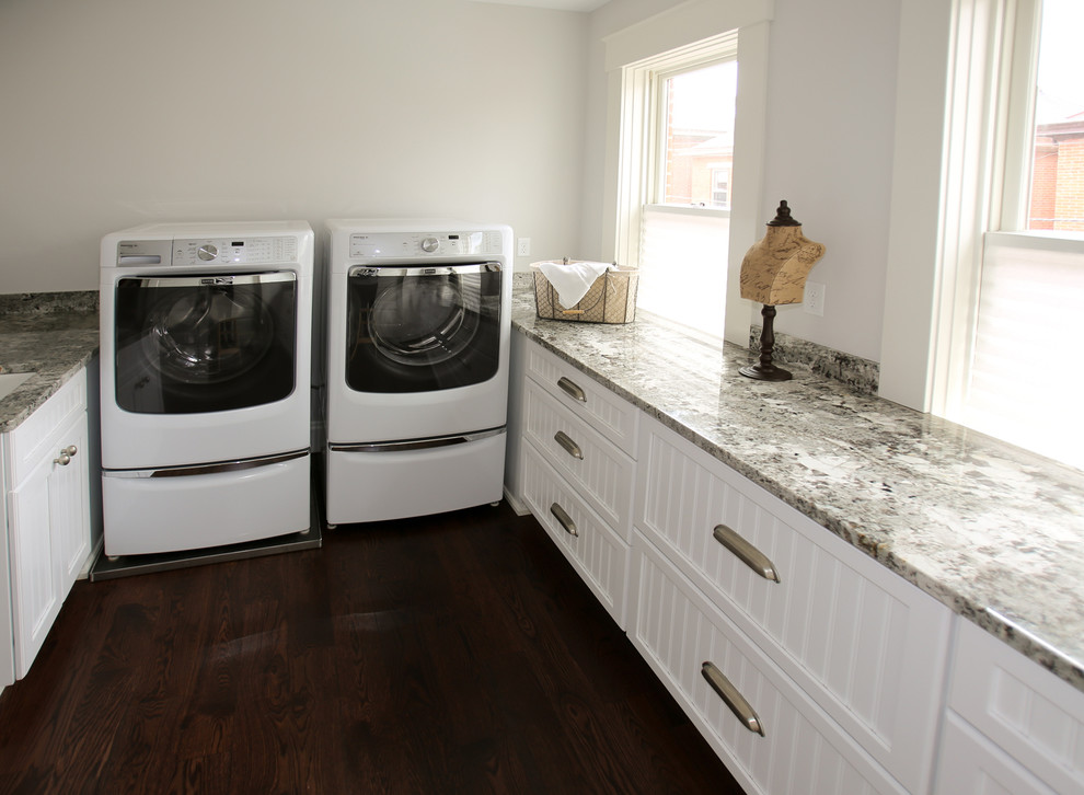 Klassische Waschküche in U-Form mit Unterbauwaschbecken, Schrankfronten im Shaker-Stil, weißen Schränken, Granit-Arbeitsplatte, dunklem Holzboden und Waschmaschine und Trockner nebeneinander in Kolumbus