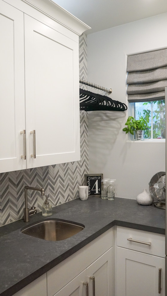 Small transitional l-shaped porcelain tile and gray floor dedicated laundry room photo in Phoenix with an undermount sink, shaker cabinets, white cabinets, quartz countertops, gray walls, a stacked washer/dryer and gray countertops