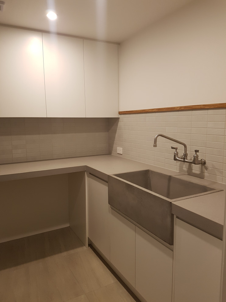 Design ideas for a small contemporary l-shaped separated utility room in Geelong with a belfast sink, white cabinets, concrete worktops, grey splashback, ceramic splashback, white walls, a side by side washer and dryer and grey worktops.
