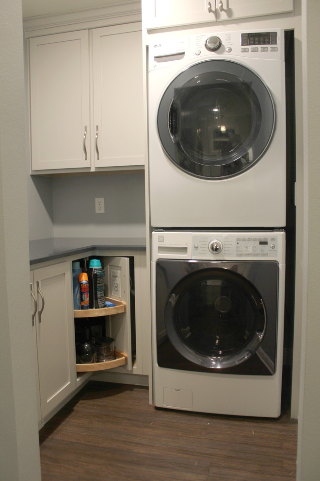 他の地域にある低価格の小さなトランジショナルスタイルのおしゃれな洗濯室 (L型、シェーカースタイル扉のキャビネット、クオーツストーンカウンター、白いキッチンパネル、セラミックタイルのキッチンパネル、クッションフロア、茶色い床、青いキッチンカウンター、グレーのキャビネット、青い壁、上下配置の洗濯機・乾燥機) の写真