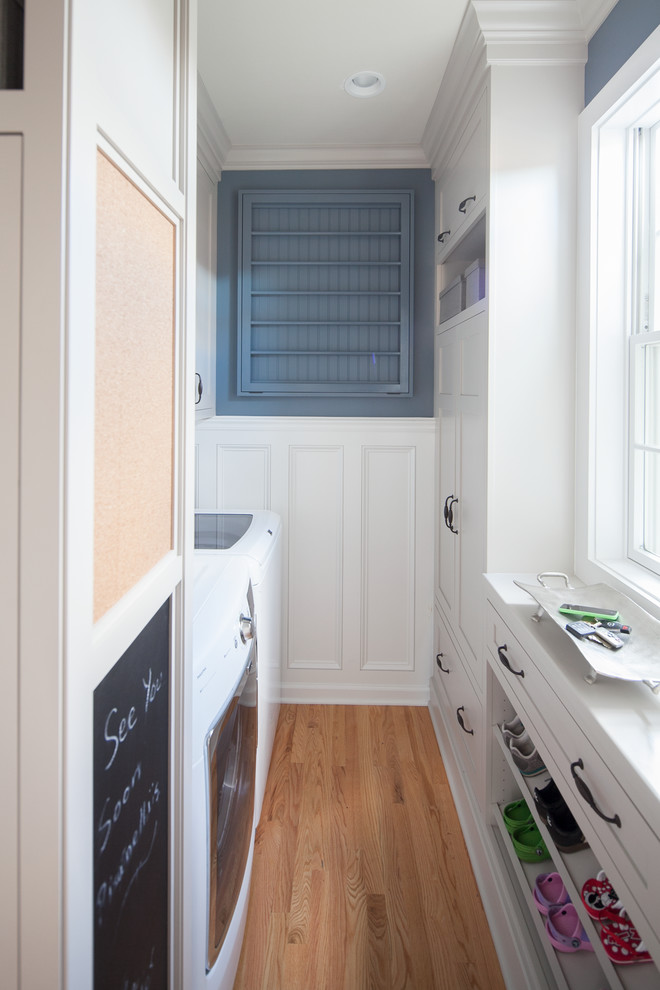 Foto di una piccola lavanderia multiuso classica con ante con riquadro incassato, ante bianche, pareti blu, pavimento in legno massello medio e lavatrice e asciugatrice affiancate