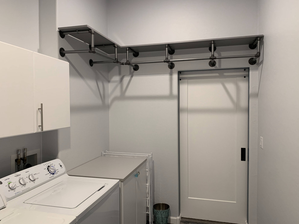 Exemple d'une buanderie parallèle industrielle dédiée avec un placard à porte plane, des portes de placard blanches, un mur gris, des machines côte à côte et un plan de travail gris.