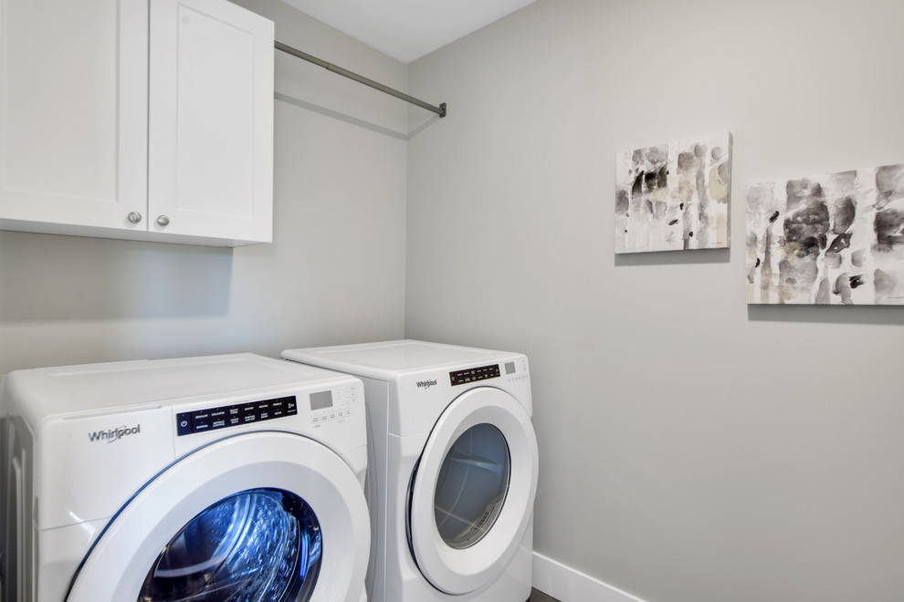 Bild på en liten amerikansk tvättstuga enbart för tvätt, med skåp i shakerstil, vita skåp, grå väggar och en tvättmaskin och torktumlare bredvid varandra