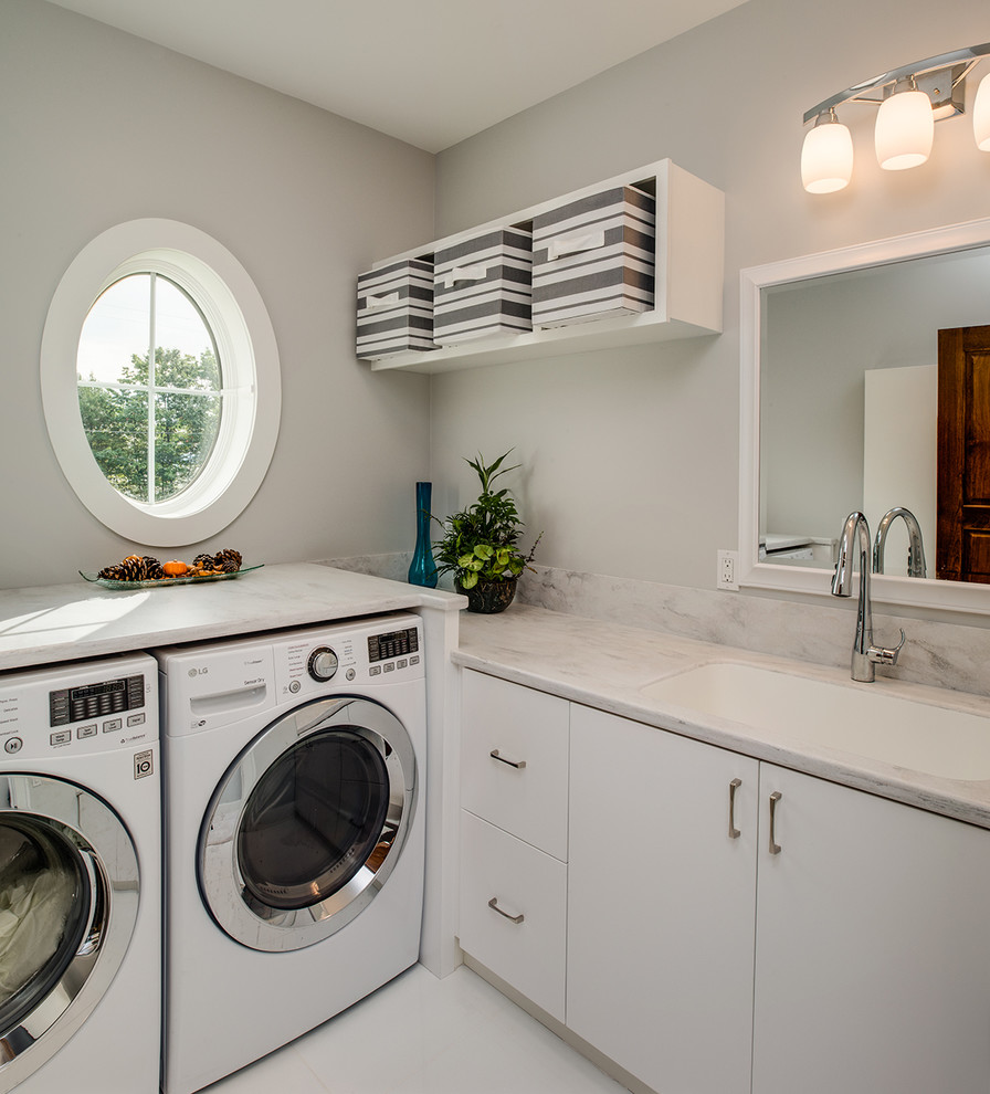 Exempel på en liten modern l-formad tvättstuga enbart för tvätt, med släta luckor, vita skåp, bänkskiva i koppar, grå väggar, klinkergolv i porslin, en tvättmaskin och torktumlare bredvid varandra och en undermonterad diskho