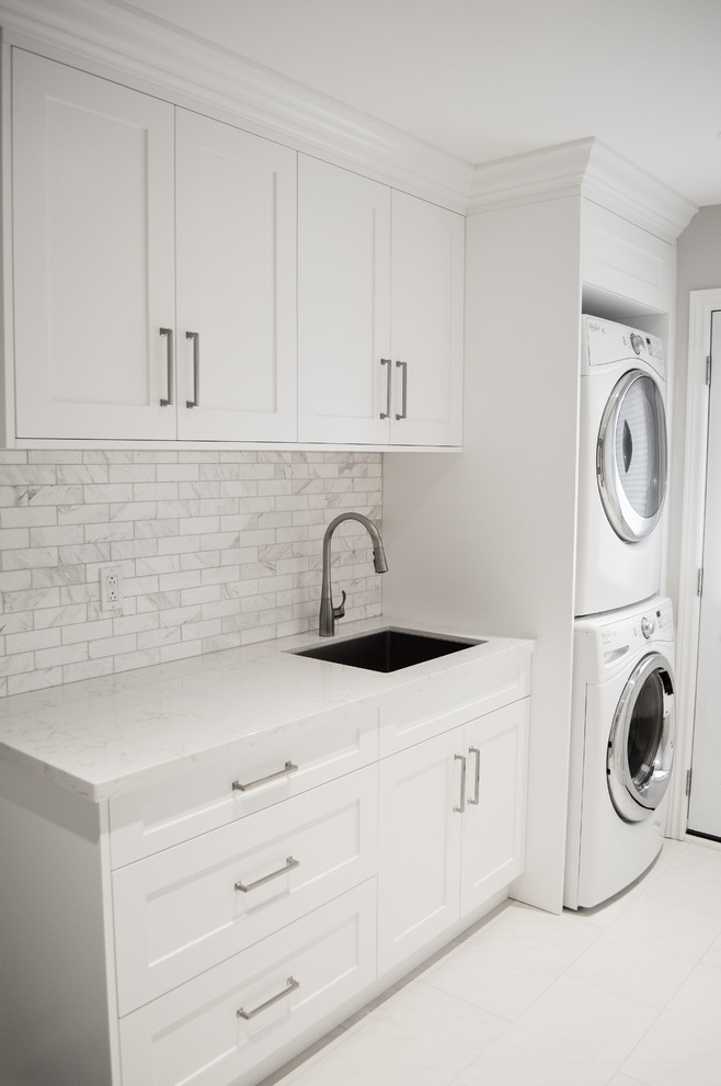 Dedicated laundry room - small transitional single-wall porcelain tile dedicated laundry room idea in Other with an undermount sink, shaker cabinets, white cabinets, quartz countertops, gray walls, a stacked washer/dryer and white countertops