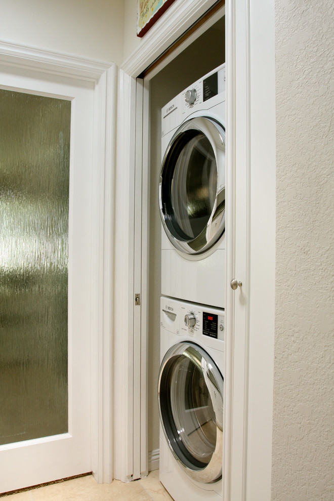 Imagen de armario lavadero de galera pequeño con armarios con paneles con relieve, puertas de armario blancas, encimera de granito, suelo de baldosas de porcelana, lavadora y secadora apiladas y suelo beige