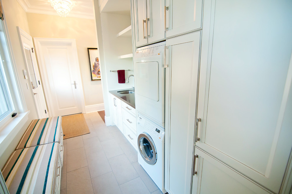 This is an example of a large classic single-wall utility room in Vancouver with a submerged sink, recessed-panel cabinets, white cabinets, composite countertops, beige walls and a stacked washer and dryer.