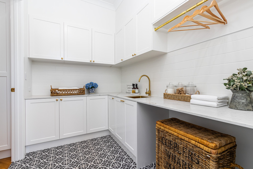 Inspiration for a coastal l-shaped black floor dedicated laundry room remodel in Townsville with an undermount sink, shaker cabinets, white cabinets, white backsplash, white walls and white countertops