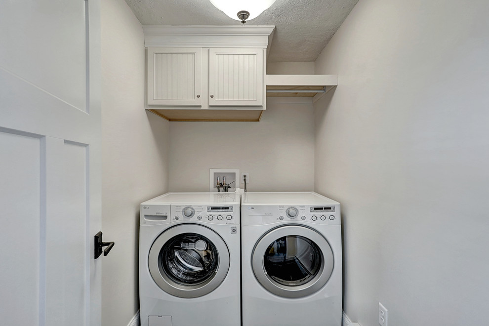 Exempel på en liten klassisk linjär liten tvättstuga, med skåp i shakerstil, vita skåp, beige väggar, laminatgolv, en tvättmaskin och torktumlare bredvid varandra och grått golv
