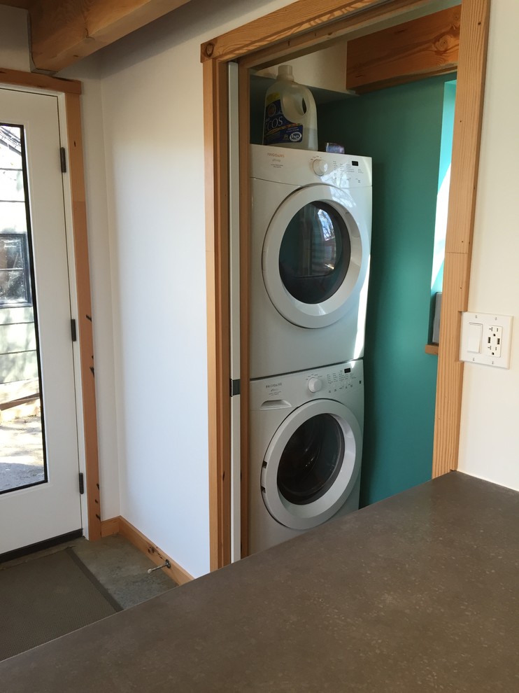 Esempio di un piccolo ripostiglio-lavanderia minimalista con pareti verdi, pavimento in cemento e lavatrice e asciugatrice a colonna