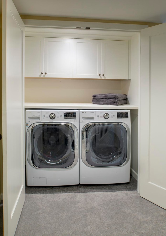 Diseño de armario lavadero lineal de estilo americano pequeño con armarios estilo shaker, puertas de armario blancas, encimera de madera, suelo de cemento, lavadora y secadora juntas y paredes beige