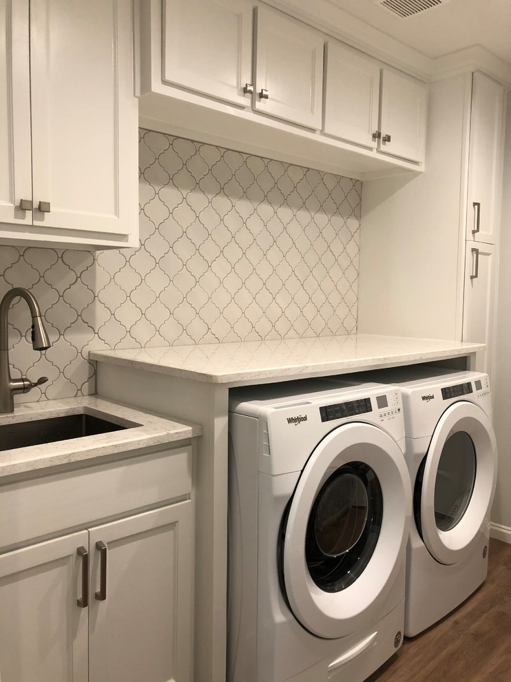 Idéer för att renovera en mellanstor vintage vita linjär vitt tvättstuga enbart för tvätt, med en undermonterad diskho, luckor med infälld panel, vita skåp, granitbänkskiva, vita väggar, mellanmörkt trägolv, en tvättmaskin och torktumlare bredvid varandra och brunt golv