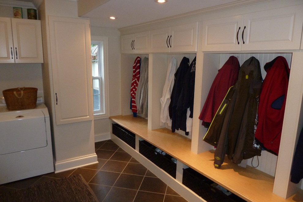 他の地域にある中くらいなコンテンポラリースタイルのおしゃれな家事室 (L型、レイズドパネル扉のキャビネット、白いキャビネット、木材カウンター、白い壁、磁器タイルの床、左右配置の洗濯機・乾燥機) の写真