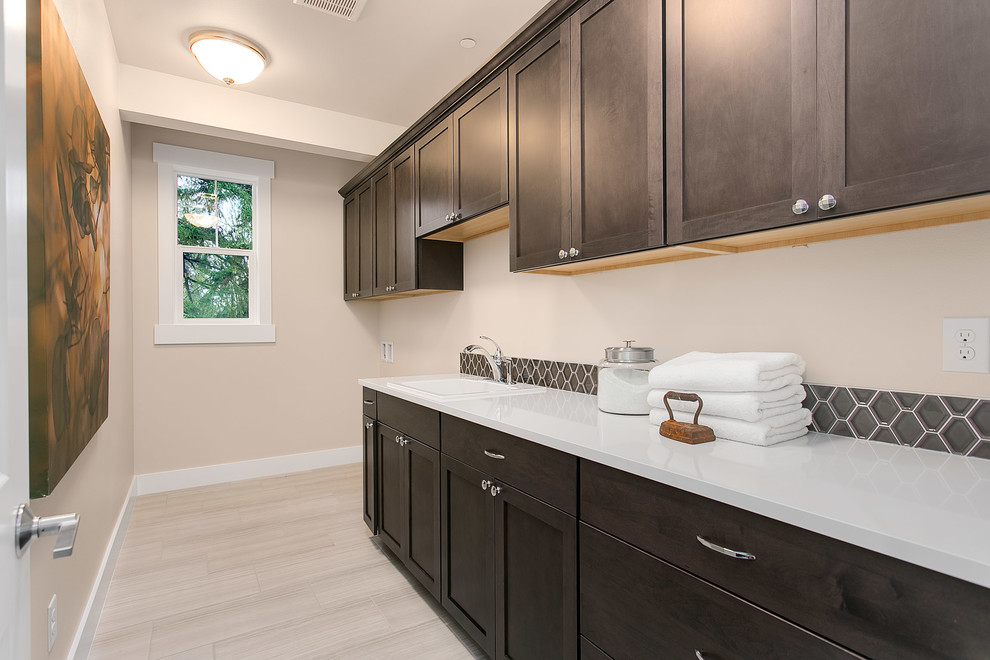 Mid-sized arts and crafts single-wall porcelain tile dedicated laundry room photo in Seattle with a drop-in sink, shaker cabinets, dark wood cabinets, solid surface countertops, beige walls and a side-by-side washer/dryer