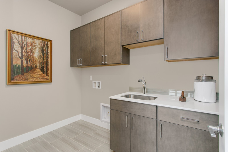 Example of a mid-sized trendy single-wall porcelain tile dedicated laundry room design in Seattle with an utility sink, flat-panel cabinets, medium tone wood cabinets, quartz countertops, gray walls and a side-by-side washer/dryer