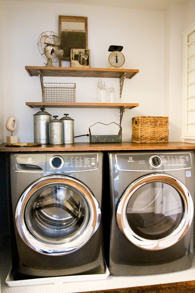 Inredning av en lantlig mellanstor bruna linjär brunt tvättstuga enbart för tvätt, med öppna hyllor, blå skåp, träbänkskiva, grå väggar, klinkergolv i keramik, en tvättmaskin och torktumlare bredvid varandra och vitt golv