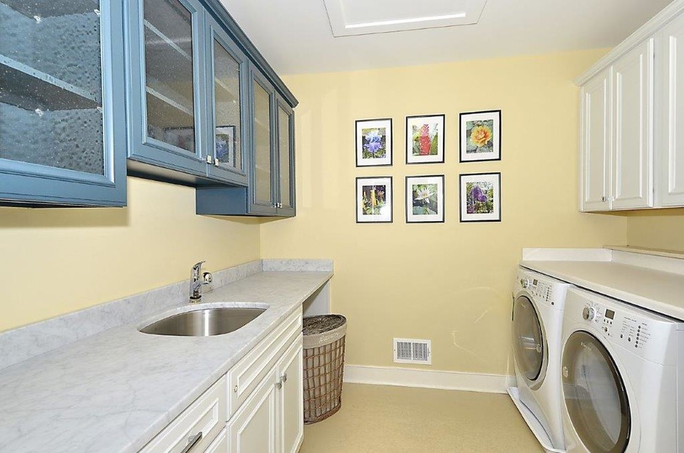 Exempel på en mellanstor klassisk parallell tvättstuga enbart för tvätt, med en undermonterad diskho, luckor med infälld panel, vita skåp, marmorbänkskiva, gula väggar och en tvättmaskin och torktumlare bredvid varandra