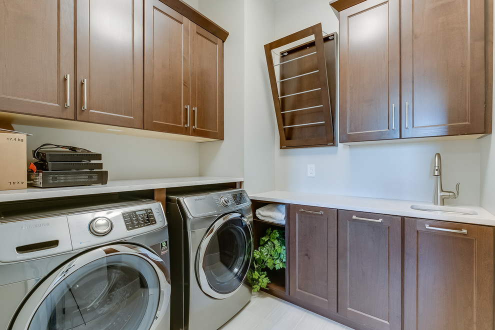 Imagen de lavadero en L clásico con fregadero bajoencimera, puertas de armario de madera en tonos medios, lavadora y secadora juntas y armarios con paneles empotrados