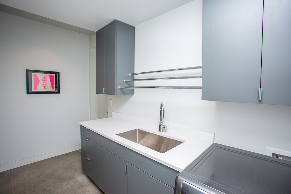Mid-sized 1960s single-wall concrete floor and beige floor dedicated laundry room photo in Portland with an undermount sink, flat-panel cabinets, gray cabinets, white walls, a side-by-side washer/dryer and white countertops