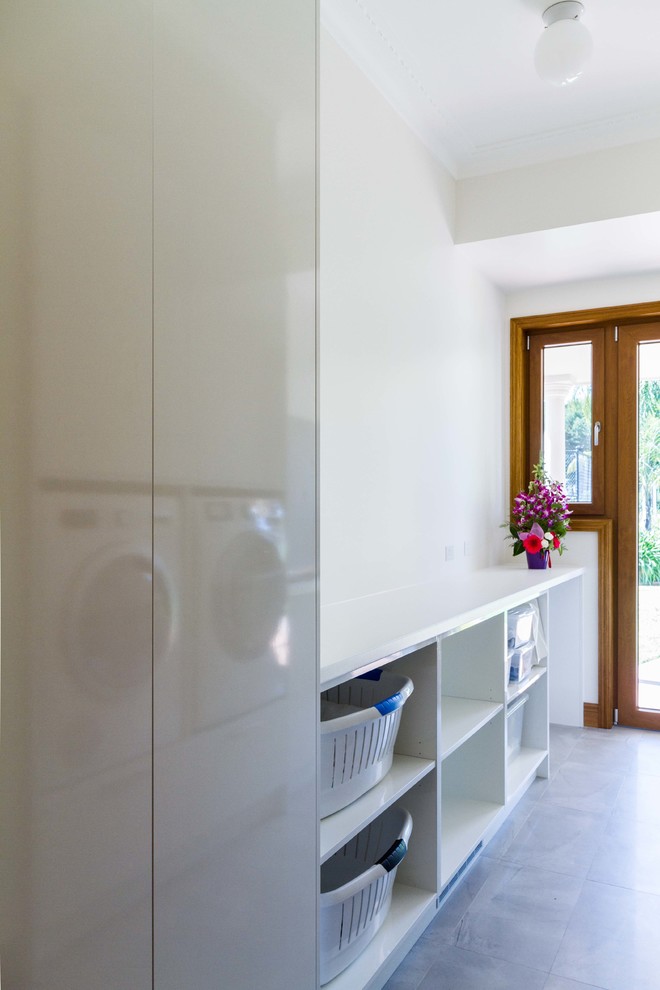 Example of a mid-sized trendy galley porcelain tile dedicated laundry room design in Melbourne with flat-panel cabinets, white cabinets, laminate countertops, white walls and a side-by-side washer/dryer