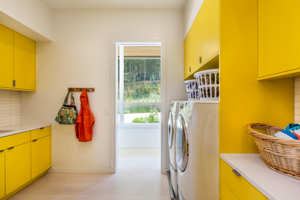 Imagen de cuarto de lavado de galera actual con armarios con paneles lisos, puertas de armario amarillas, encimera de cuarzo compacto, paredes blancas, lavadora y secadora juntas y suelo de madera clara