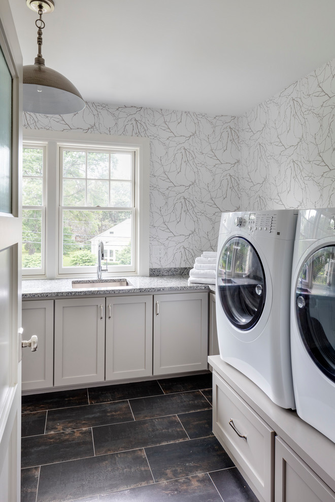 Bild på en mellanstor vintage grå l-formad grått tvättstuga, med granitbänkskiva, klinkergolv i keramik, en tvättmaskin och torktumlare bredvid varandra, svart golv, en undermonterad diskho, skåp i shakerstil, vita skåp och vita väggar
