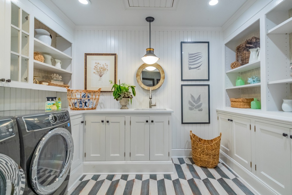 Bild på en vintage vita u-formad vitt tvättstuga, med en undermonterad diskho, luckor med infälld panel, vita skåp, vita väggar, en tvättmaskin och torktumlare bredvid varandra och flerfärgat golv