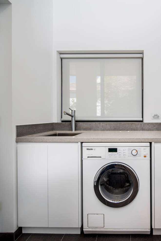 Foto på en liten nordisk linjär tvättstuga enbart för tvätt, med en undermonterad diskho, släta luckor, vita skåp, bänkskiva i kvarts, vita väggar och klinkergolv i porslin