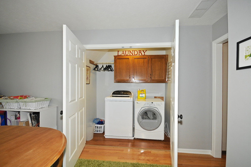 Foto på en mellanstor funkis linjär liten tvättstuga, med luckor med infälld panel, skåp i mellenmörkt trä, grå väggar, mellanmörkt trägolv och en tvättmaskin och torktumlare bredvid varandra