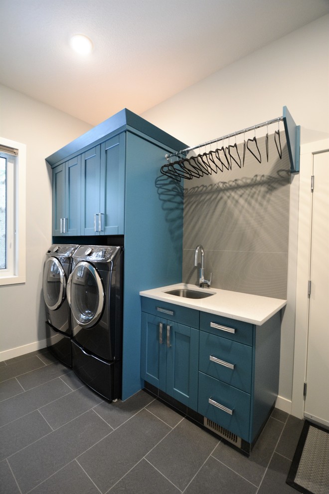 Esempio di una sala lavanderia chic di medie dimensioni con lavello sottopiano, ante in stile shaker, ante blu, top in quarzo composito, pareti grigie, pavimento in gres porcellanato, lavatrice e asciugatrice affiancate e pavimento grigio