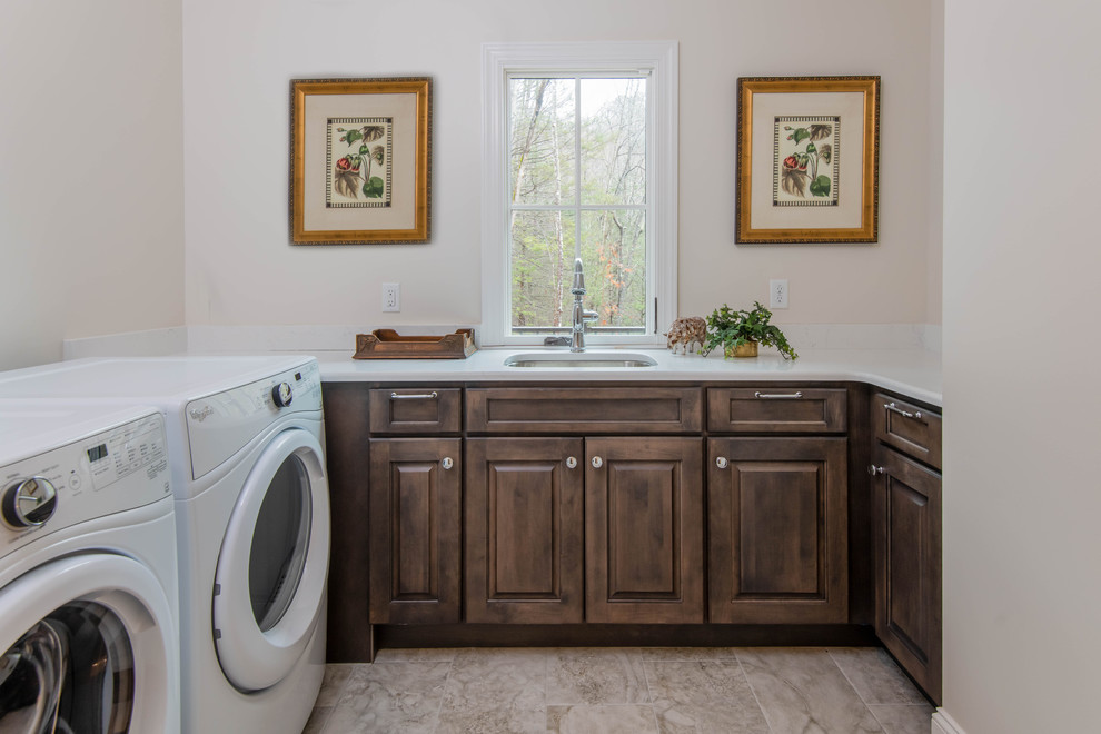 Inspiration för små klassiska u-formade vitt tvättstugor enbart för tvätt, med en undermonterad diskho, luckor med upphöjd panel, bruna skåp, beige väggar, klinkergolv i keramik, en tvättmaskin och torktumlare bredvid varandra och brunt golv