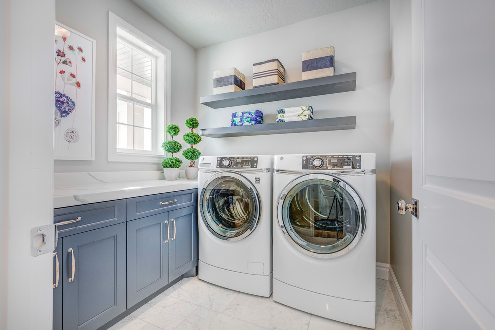 Diseño de lavadero tradicional con armarios con paneles empotrados, puertas de armario azules, paredes blancas, lavadora y secadora juntas, suelo blanco y encimeras blancas