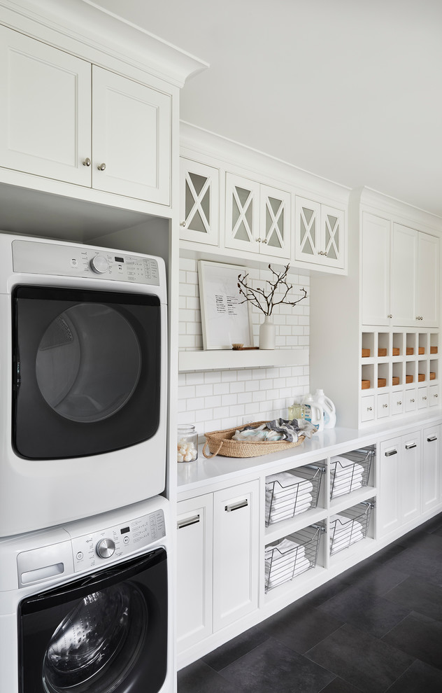 Beach style black floor dedicated laundry room photo in Dallas with shaker cabinets, white cabinets, a stacked washer/dryer and white countertops