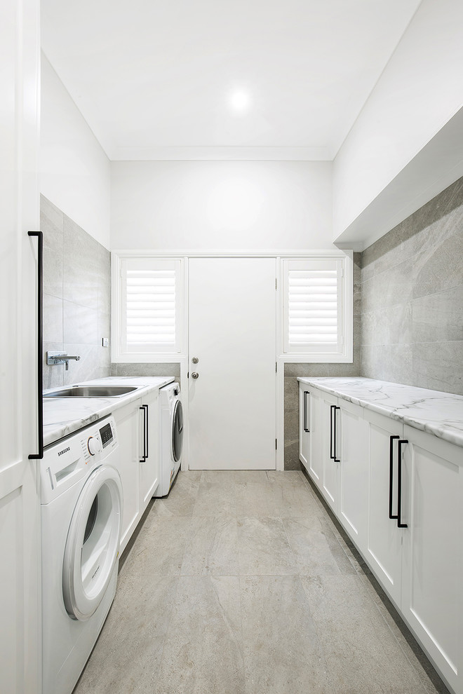 Modern inredning av en mellanstor parallell tvättstuga enbart för tvätt, med en nedsänkt diskho, skåp i shakerstil, vita skåp, laminatbänkskiva, grå väggar, klinkergolv i keramik, en tvättmaskin och torktumlare bredvid varandra och grått golv
