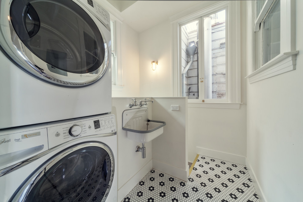 Foto de lavadero multiusos clásico de tamaño medio con pila para lavar, paredes blancas, suelo de baldosas de cerámica y lavadora y secadora apiladas