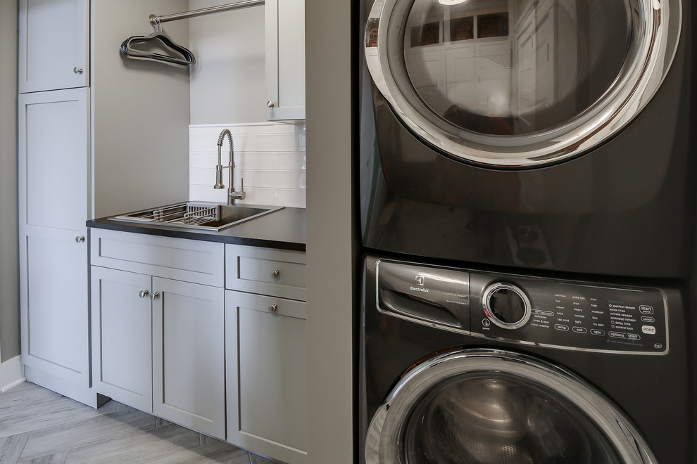Inspiration for a small traditional single-wall separated utility room in Dallas with a built-in sink, shaker cabinets, grey cabinets, engineered stone countertops, grey walls, laminate floors, a stacked washer and dryer, grey floors and black worktops.