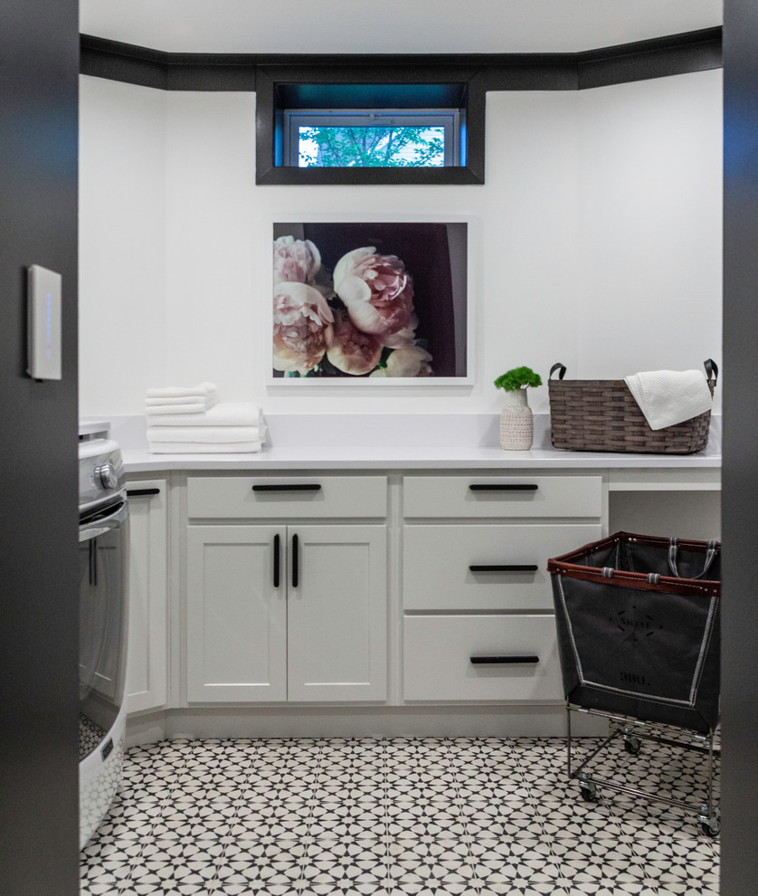 Inredning av en klassisk vita l-formad vitt tvättstuga, med skåp i shakerstil, grå skåp, vita väggar, en tvättmaskin och torktumlare bredvid varandra, bänkskiva i koppar, klinkergolv i porslin och vitt golv