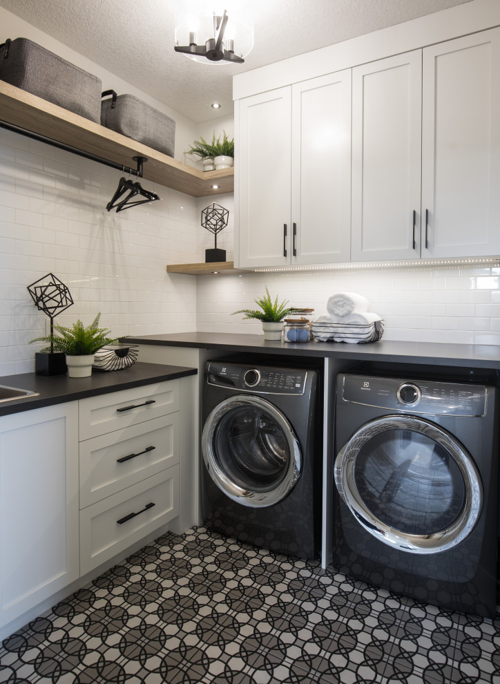 Mittelgroße Klassische Waschküche in L-Form mit Schrankfronten im Shaker-Stil, weißen Schränken, Laminat-Arbeitsplatte, Waschmaschine und Trockner nebeneinander und schwarzer Arbeitsplatte in Calgary