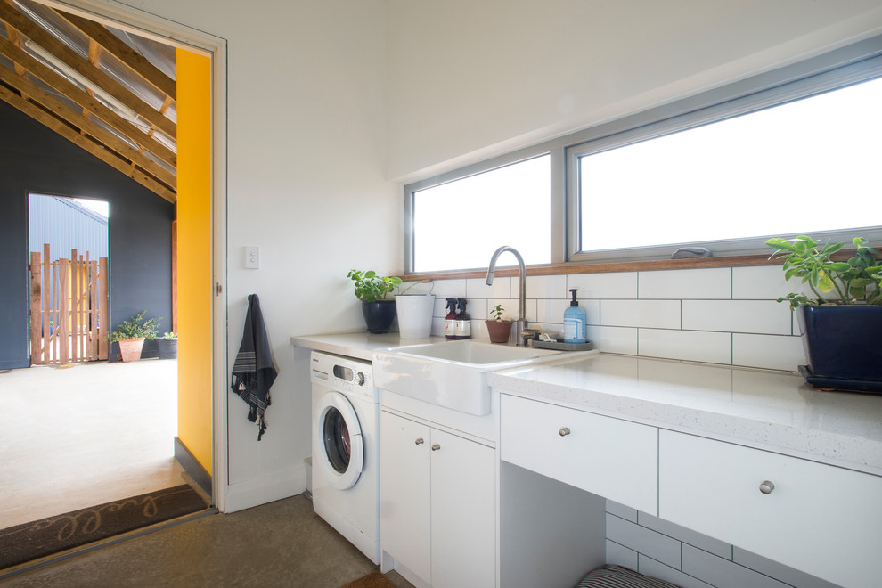 Modelo de cuarto de lavado lineal contemporáneo con fregadero sobremueble, armarios con paneles lisos, puertas de armario blancas, paredes blancas, suelo de cemento, suelo gris y encimeras blancas