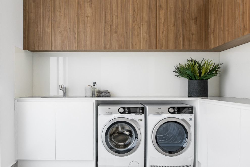 Modelo de lavadero en L contemporáneo con armarios con paneles lisos, puertas de armario blancas, paredes blancas, lavadora y secadora juntas y encimeras blancas